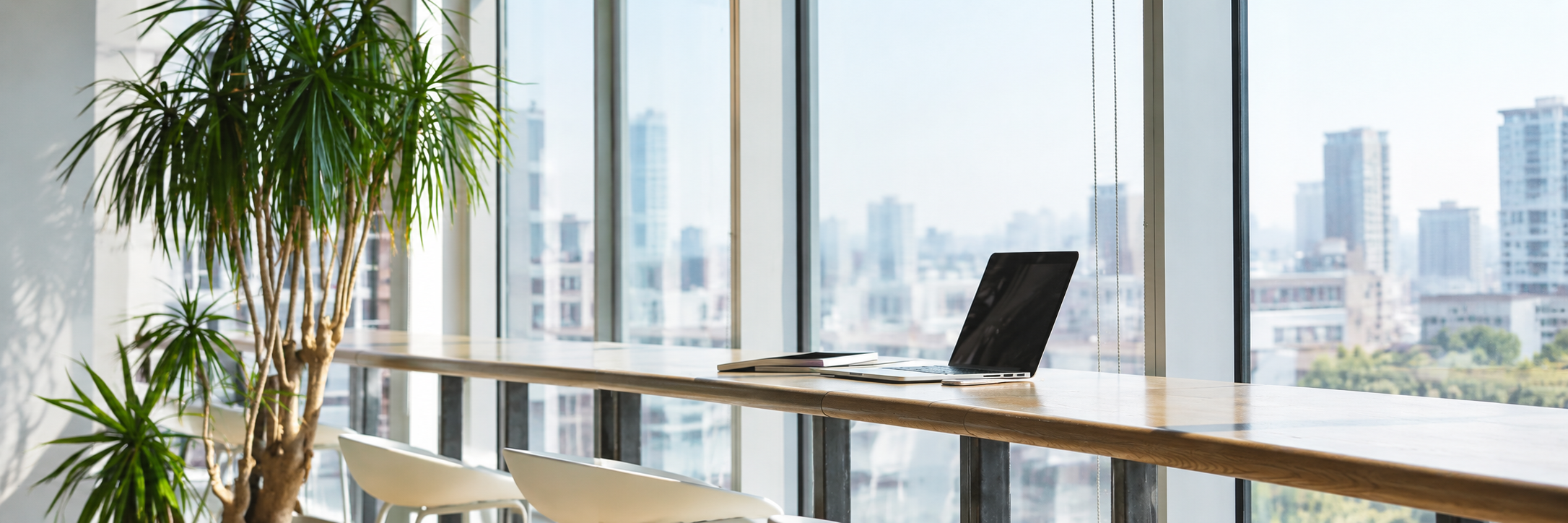 Bright workspace with a laptop beside large windows overlooking the city